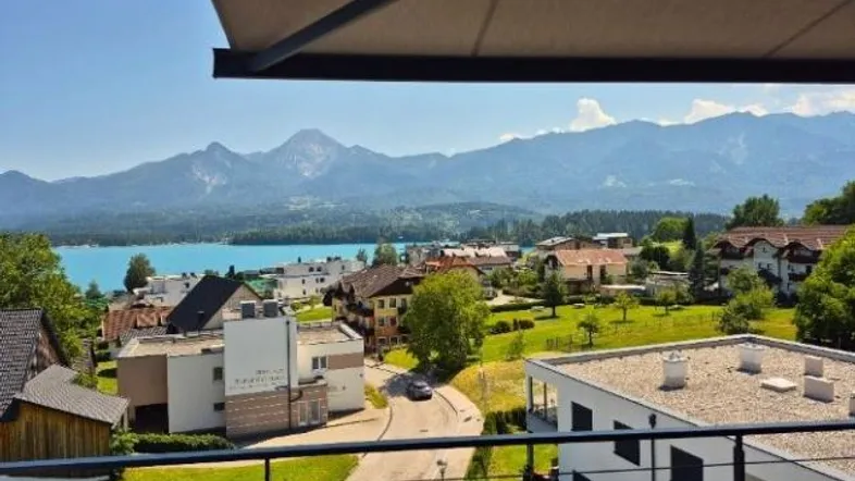 Panoramablick von einem Balkon auf einen türkisfarbenen See und die umliegende Berglandschaft.
