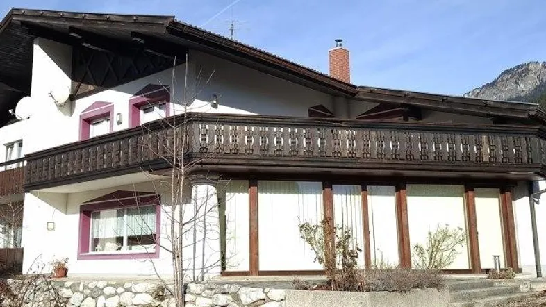 Traditionelles Haus mit Holzbalkon und Blick auf die Berge unter blauem Himmel.