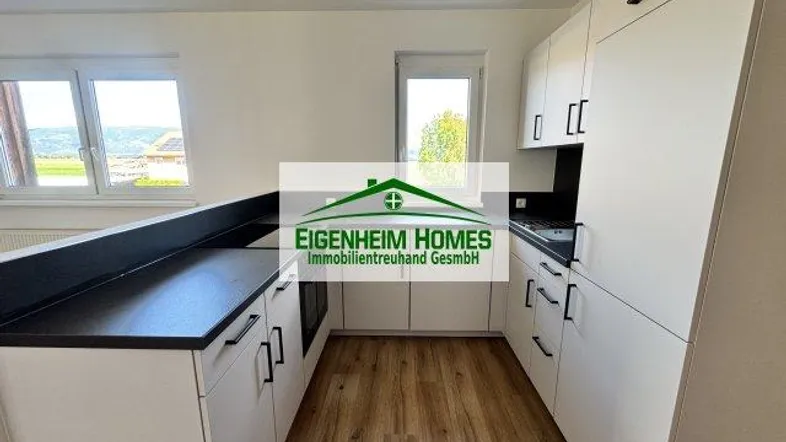 Moderne Küche mit weißen Schränken, dunkler Arbeitsplatte und Blick ins Grüne.