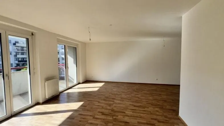 Helles Wohnzimmer mit Parkettboden und Zugang zu einem Balkon, durchflutet von natürlichem Sonnenlicht.