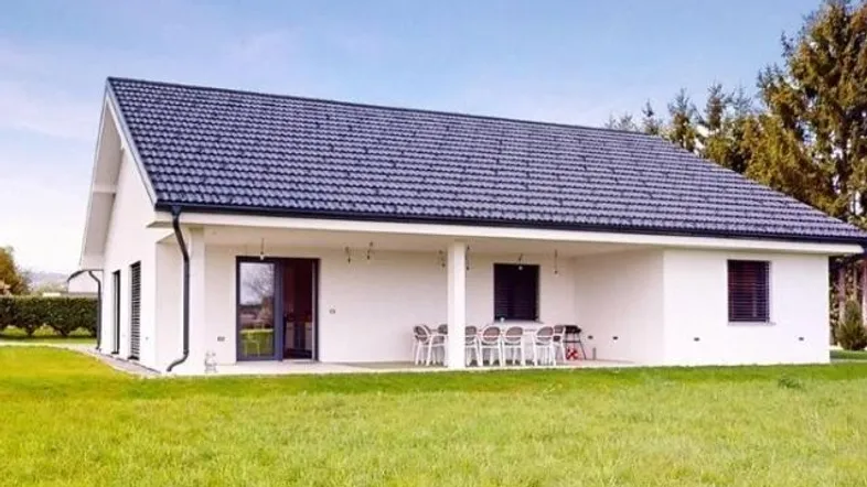Modernes Einfamilienhaus mit weißer Fassade, dunklem Dach und überdachter Terrasse im Grünen.