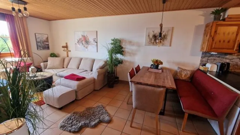 Gemütlicher Wohn- und Essbereich mit beiger Couch, Holzbalkendecke und rustikalen Fliesenboden.