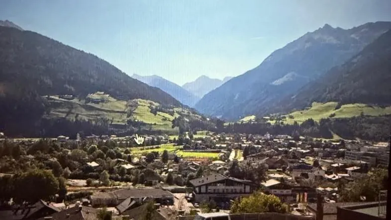 Panoramablick auf ein malerisches Tal mit einer Siedlung und majestätischen Bergen im Hintergrund.