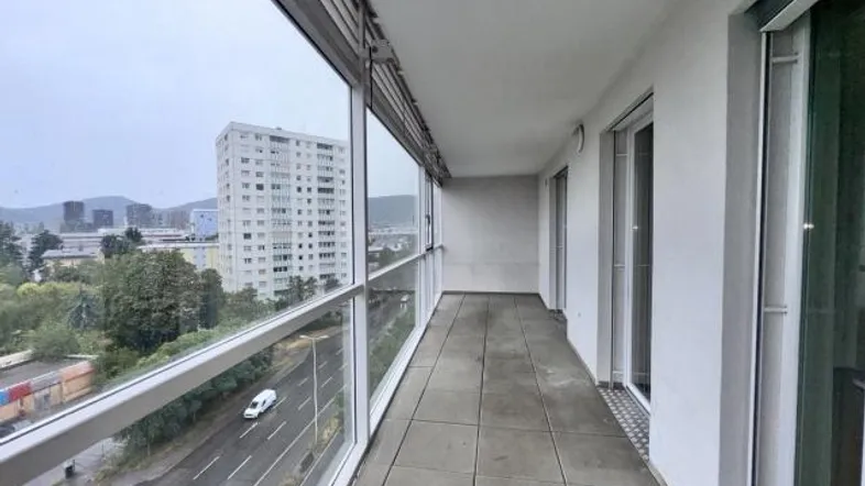 Langer Balkon mit Glasbrüstung und weitem Blick auf die Stadt und umliegende Gebäude.