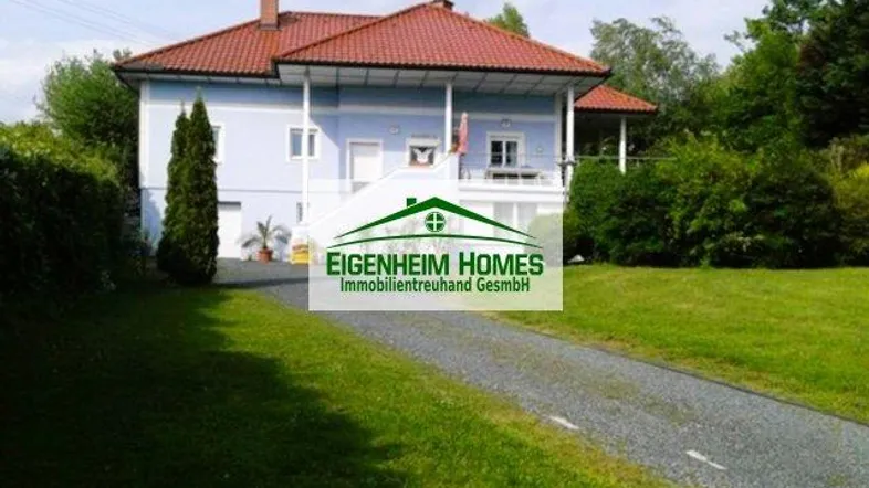 Freistehendes Haus mit hellblauer Fassade, rotem Satteldach, Balkon und großem Garten mit Kiesauffahrt.