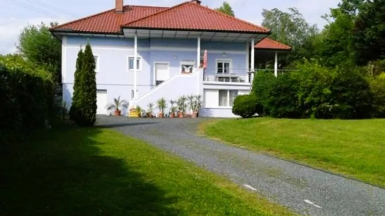 Einfamilienhaus mit hellblauer Fassade, rotem Ziegeldach, Kiesauffahrt und gepflegtem Vorgarten.