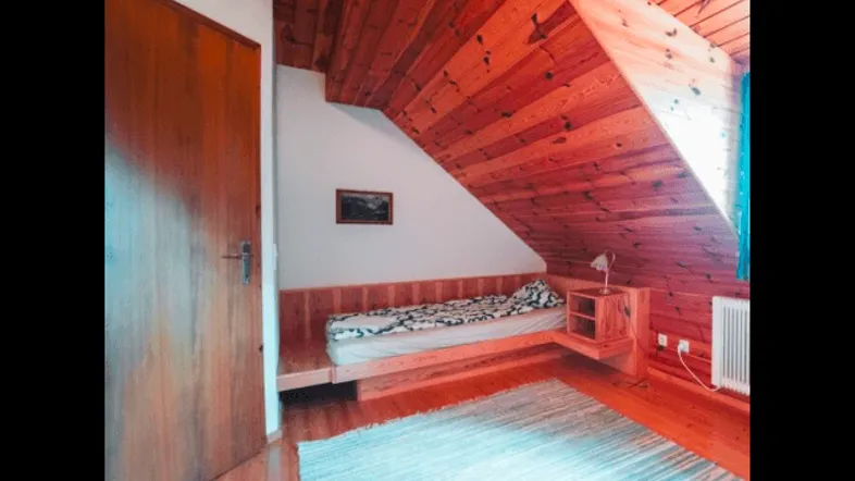 Schlafzimmer mit Holzboden, Holzdecke und Dachschräge, ausgestattet mit einem Einzelbett.