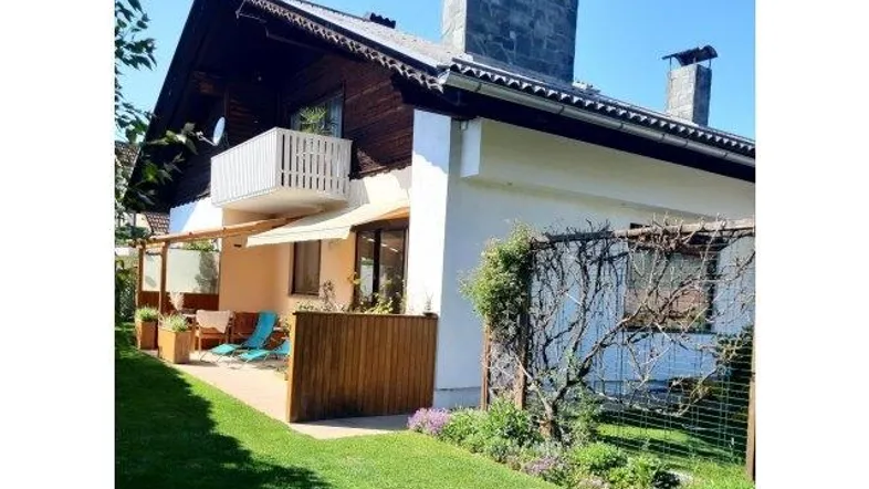 Charmantes Einfamilienhaus mit Balkon, Terrasse und gepflegtem Gartenbereich unter blauem Himmel.