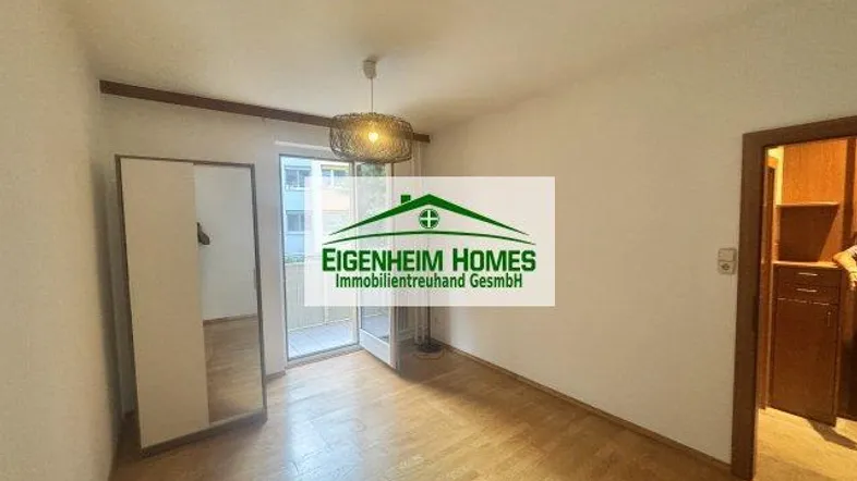 Helles Zimmer mit Parkettboden, Zugang zum Balkon und einem modernen Deckenlicht.