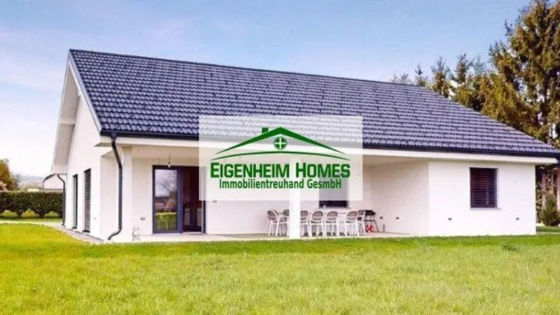 Modernes Einfamilienhaus mit weißer Fassade, dunklem Dach und einer möblierten Terrasse im Grünen.