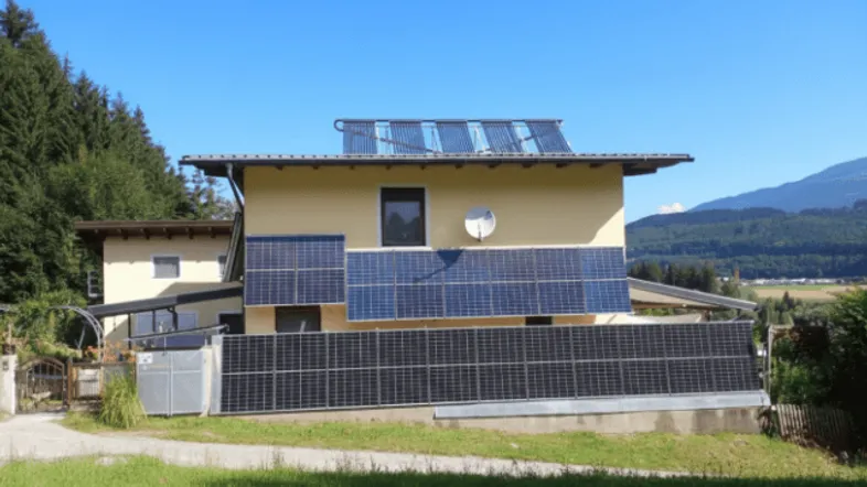 Hausfassade mit zahlreichen Photovoltaik- und Solaranlagen auf Dach und Wand, umgeben von grüner Natur.