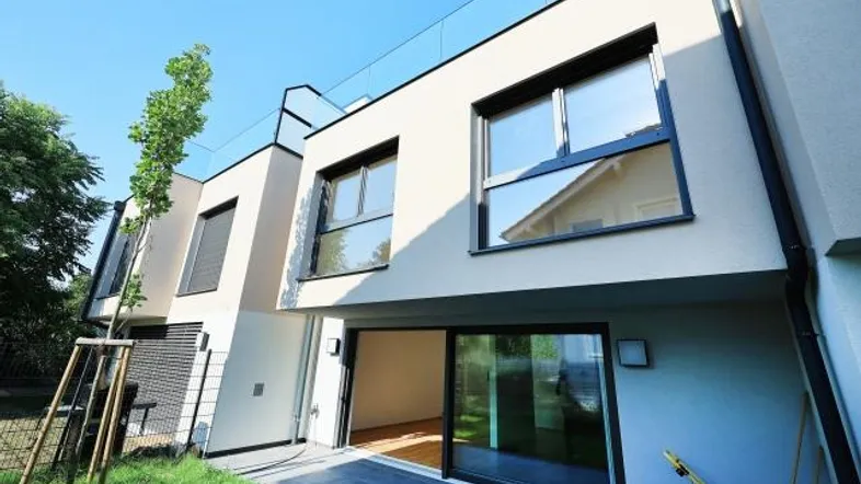 Moderne Reihenhausfassade mit großer Glasschiebetür, kleiner Terrasse und Gartenbereich.