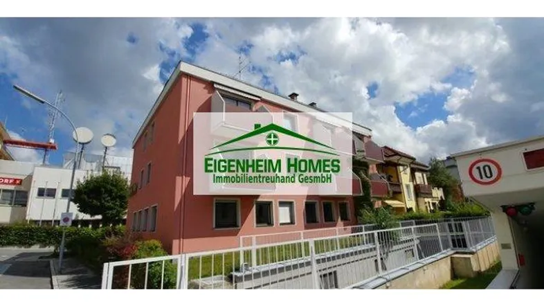 Gebäudeansicht eines Mehrfamilienhauses mit rosa Fassade und Zufahrt zur Tiefgarage.
