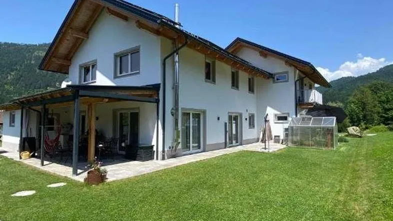 Modernes Einfamilienhaus mit großem Garten, überdachter Terrasse und Bergblick.