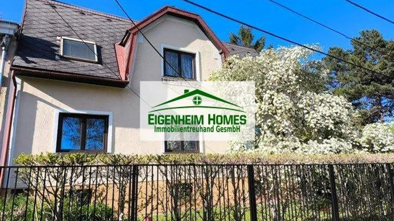 Vorderansicht des Hauses mit Mansarddach und gepflegtem Vorgarten hinter einem Zaun.