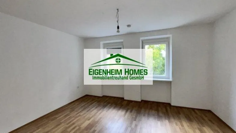 Heller, leerer Raum mit Holzboden und zwei Fenstern, bereit zur individuellen Gestaltung.