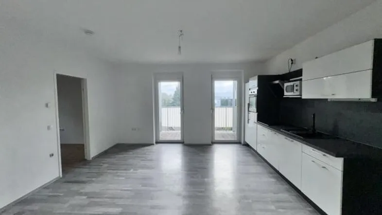 Heller offener Wohnbereich mit integrierter Küche, Laminatboden und Zugang zum Balkon.