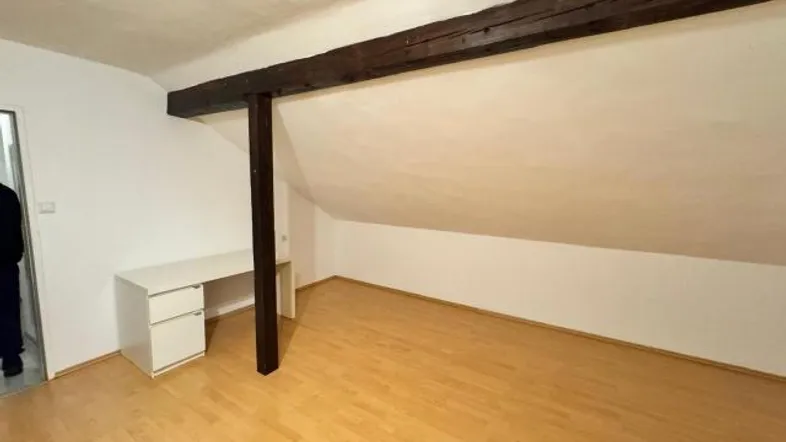 Heller Raum im Dachgeschoss mit Holzbalken, Schreibtisch und Laminatboden.