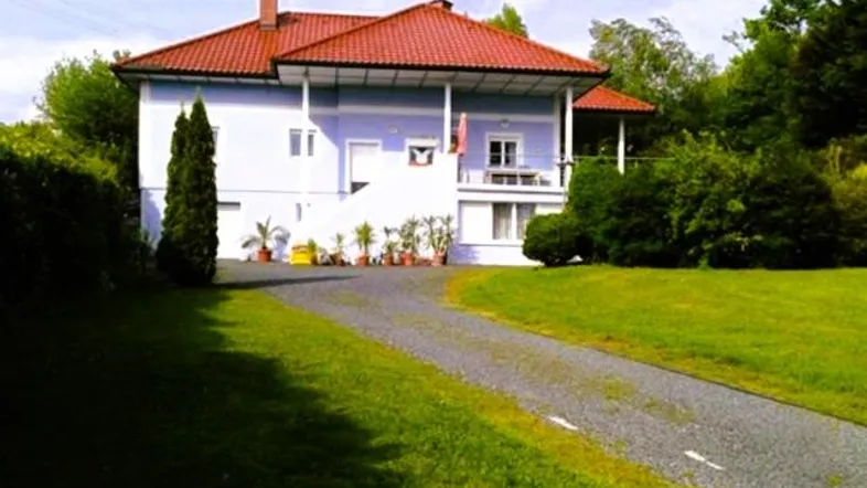 Einfamilienhaus mit hellblauer Fassade, rotem Ziegeldach und gepflegtem Vorgarten.