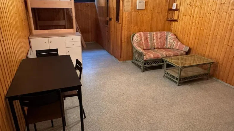Rustikaler Raum mit Holzvertäfelung, Etagenbett, Sofa und Esstisch, ideal als Gästezimmer.