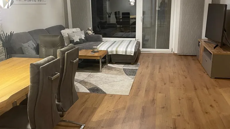 Geräumiger Wohn- und Essbereich mit Holzboden, gemütlichem Sofa und Zugang zum Balkon.