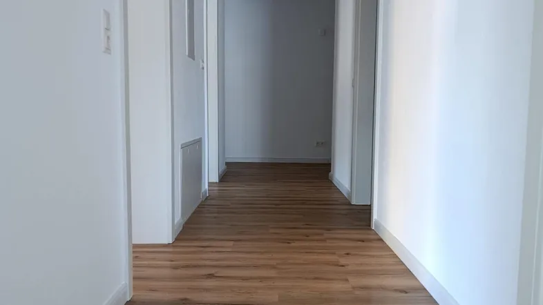 Heller Flur mit modernem Laminatboden und weißen Wänden, der zu verschiedenen Räumen führt.