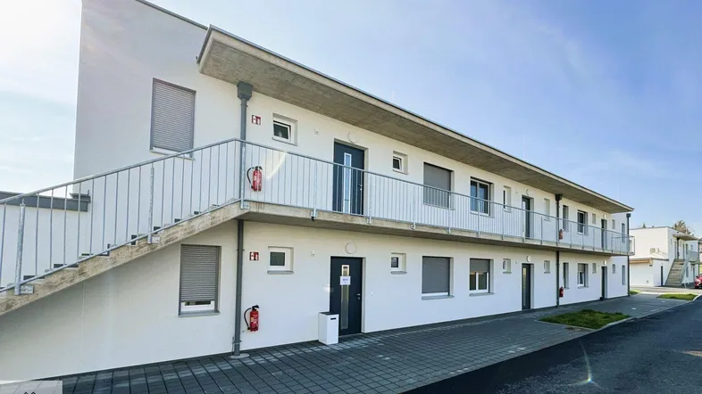 Moderne Wohnanlage mit weißer Fassade, Außentreppe und Balkonen unter blauem Himmel.