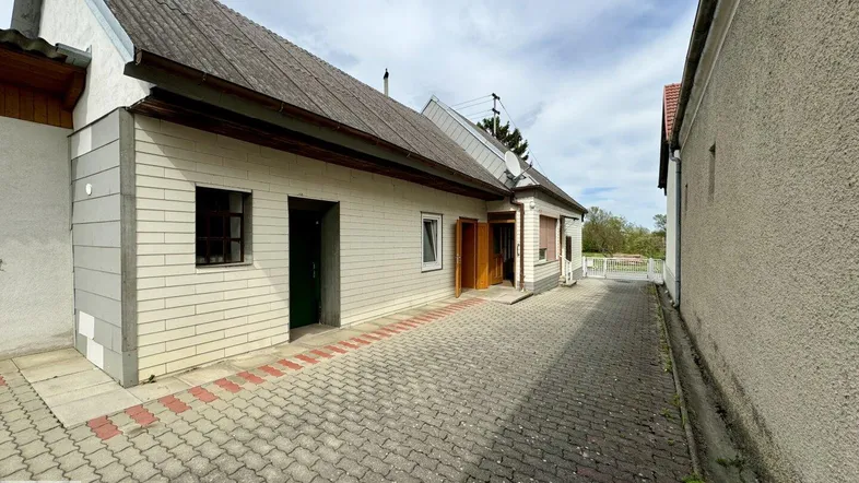 Ansicht des Hauses von der Seite mit gepflasterter Zufahrt und Eingangsbereich unter bewölktem Himmel.