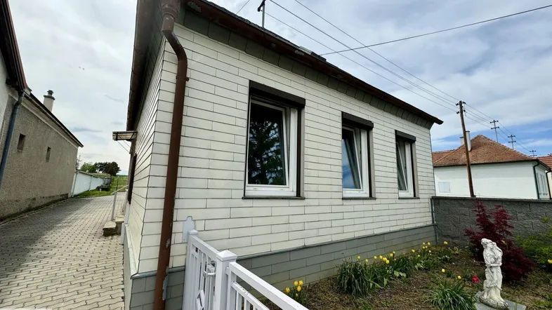 Seitenansicht eines Hauses mit weißer Fassade, Rollläden und einem kleinen Vorgarten.