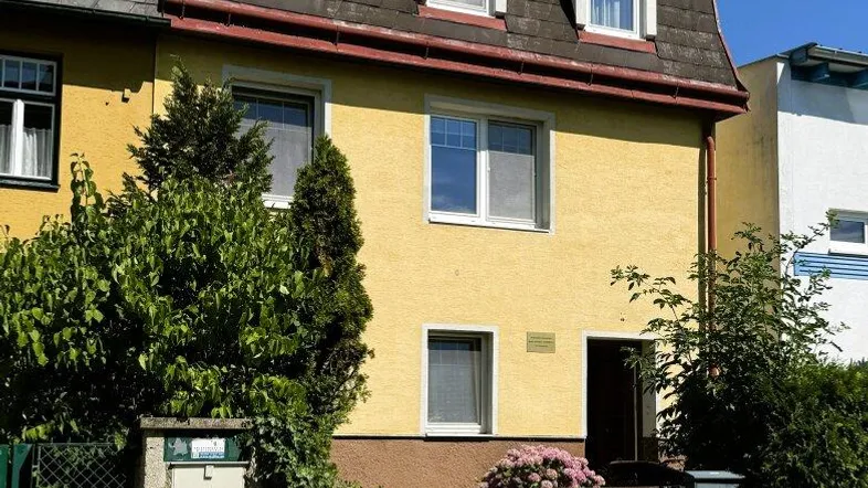 Gelbes Mehrfamilienhaus mit Mansarddach und Satellitenschüssel an einem sonnigen Tag.