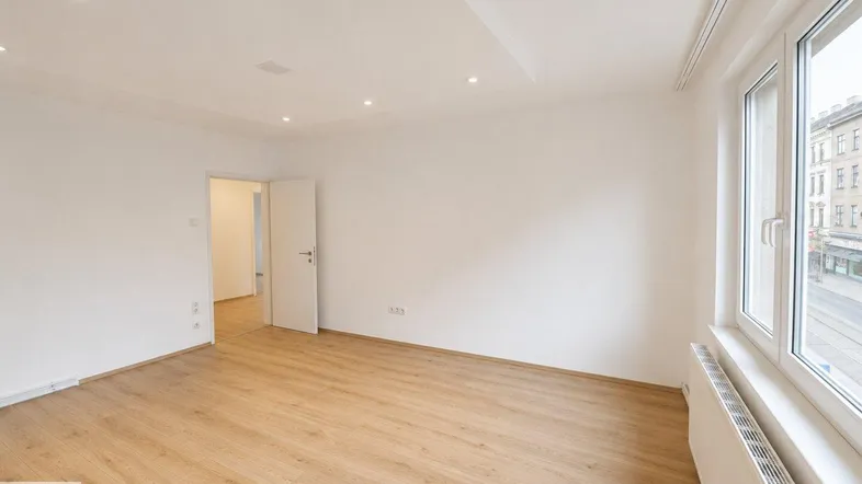 Heller, leerer Raum mit Laminatboden und großem Fenster, ideal als Wohnzimmer.