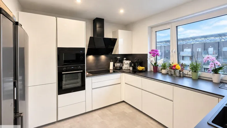 Moderne Einbauküche mit weißen Hochglanzfronten, dunkler Arbeitsplatte und Blick nach draußen.