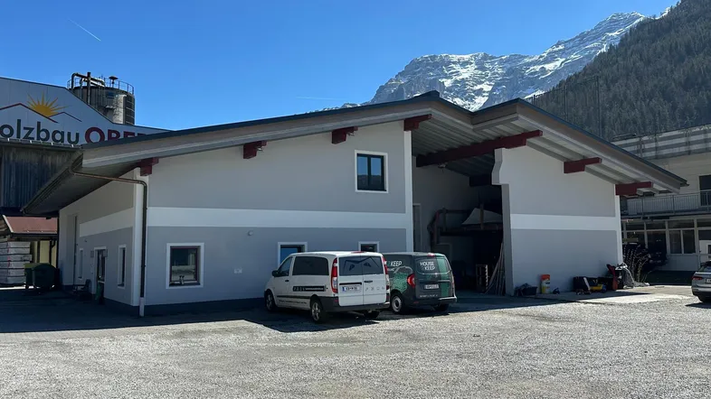 Modernes Gewerbegebäude mit grauer Fassade und roten Akzenten vor einer beeindruckenden Bergkulisse.