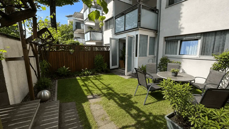 Grüner Gartenbereich mit Rasenfläche, Holzzaun und gemütlicher Sitzgelegenheit im Freien.