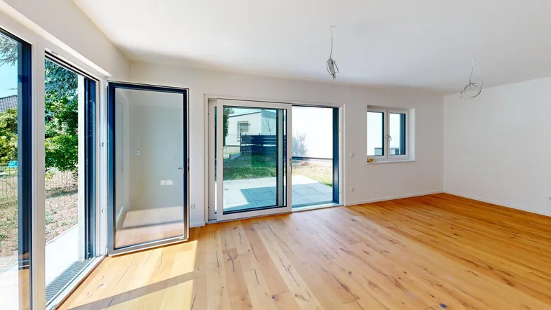 Helles, unmöbliertes Zimmer mit Holzboden und großen Glasfronten zum Garten.