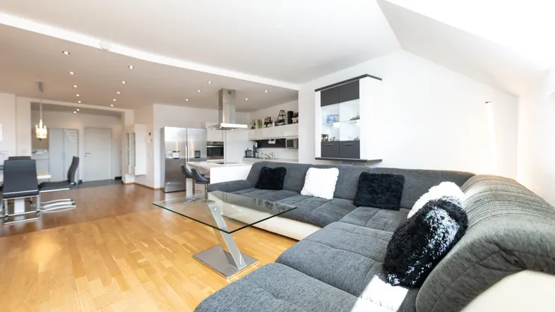 Helles, offenes Wohnzimmer mit Parkettboden, großem Sofa und Blick auf die moderne Küche.