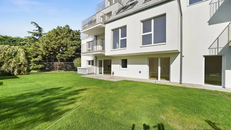 Großer, gepflegter Rasenbereich vor einem modernen Wohngebäude mit Terrassenzugang und Balkonen.