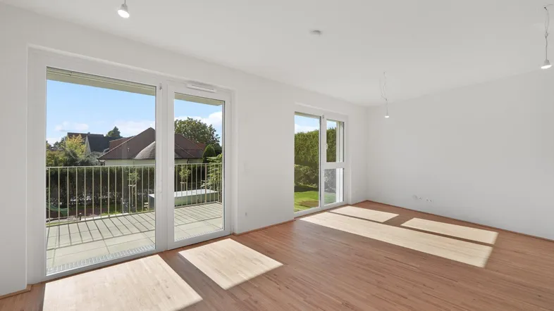 Helles Wohnzimmer mit großen Fenstern, Holzboden und Zugang zu einem Balkon.