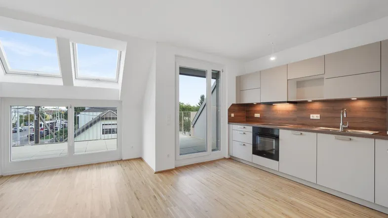 Heller offener Wohnbereich mit integrierter Küche, Holzboden und Zugang zu einer Terrasse.