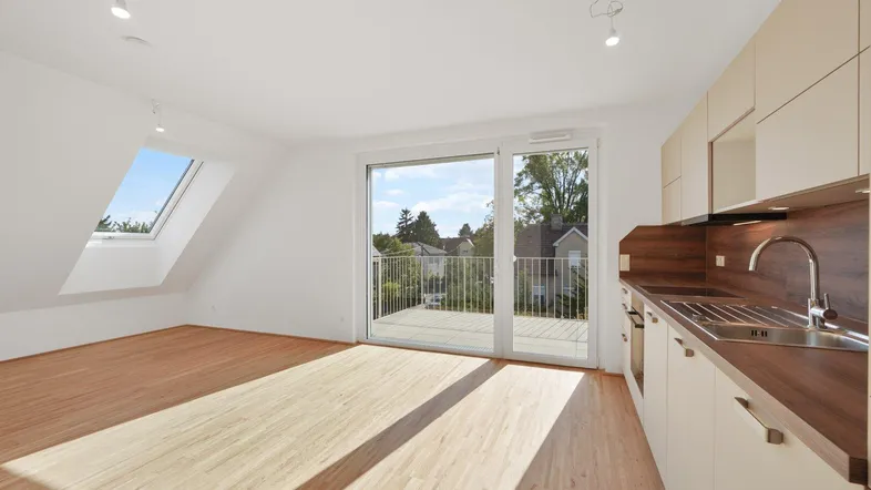 Heller offener Wohn-Essbereich mit integrierter Küche, Holzboden und Zugang zu einem Balkon.