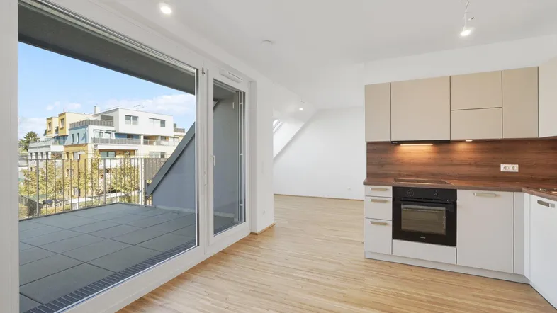 Moderne Küche mit Einbauofen und Zugang zu einer großen Terrasse mit Blick auf umliegende Gebäude.