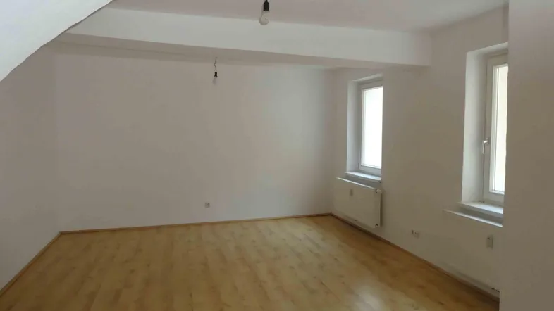 Heller, leerer Raum mit Laminatboden, zwei Fenstern und einer gewölbten Decke.