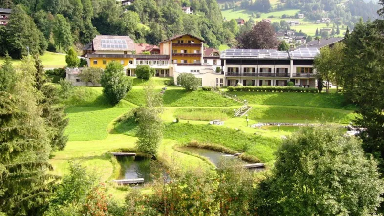 Weitläufige Anlage mit mehreren Gebäuden, grünen Wiesen, Teichen und Bergblick.