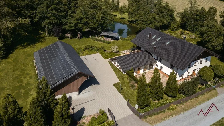Luftaufnahme des Anwesens mit Haupthaus, Nebengebäude mit Solaranlage und einem Teich im Grünen.