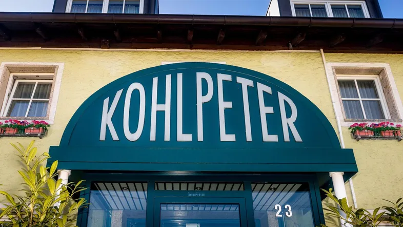 Nahaufnahme des Eingangsbereichs eines Gebäudes mit dem Schriftzug "KOHLPETER" und Blumenkästen.