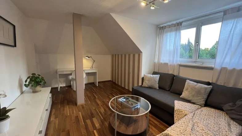 Helles Wohnzimmer im Dachgeschoss mit Holzboden, gemütlichem Sofa und integriertem Arbeitsbereich.