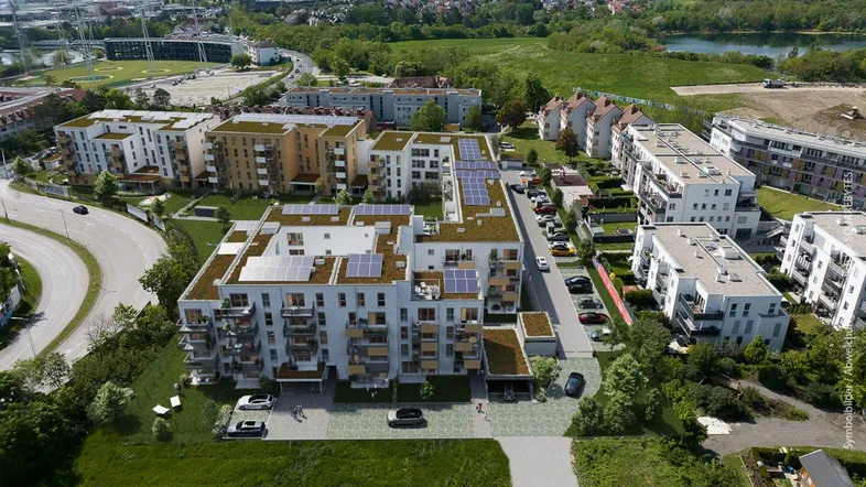 Luftaufnahme eines modernen Wohnkomplexes mit Gründächern, Solaranlagen und Balkonen in grüner Umgebung.