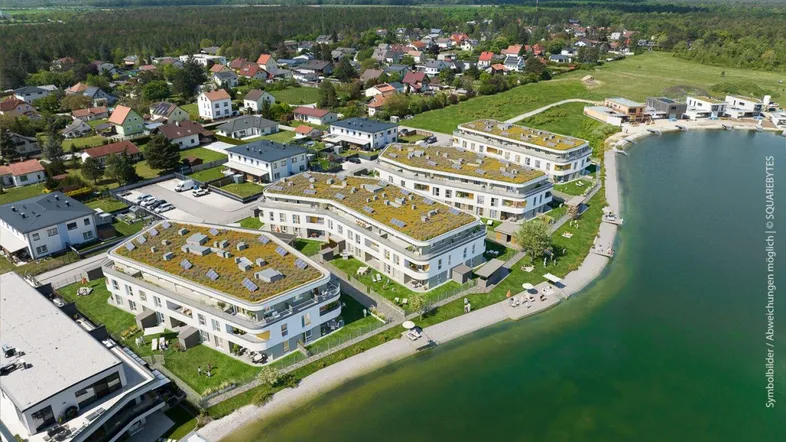 Moderne Wohngebäude mit Gründächern und Photovoltaikanlagen direkt am Seeufer mit Bergblick.