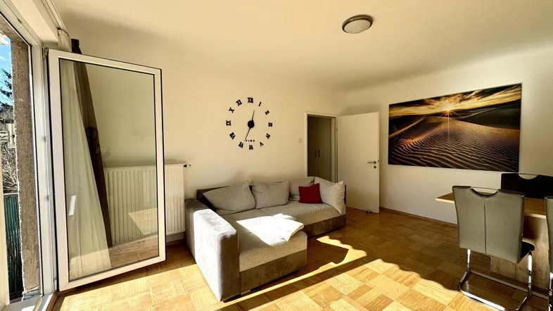 Helles Wohn- und Esszimmer mit Parkettboden, Sofa und Essbereich, sonnendurchflutet durch Balkonzugang.