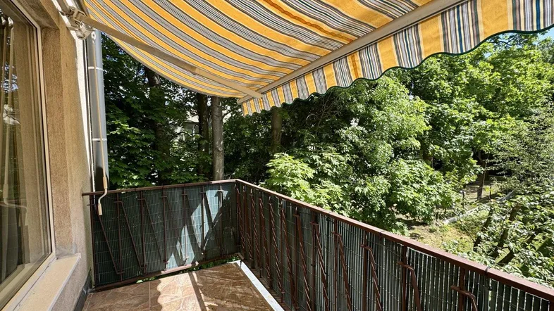 Geräumiger Balkon mit gestreifter Markise und Blick ins Grüne, ideal zum Entspannen im Freien.